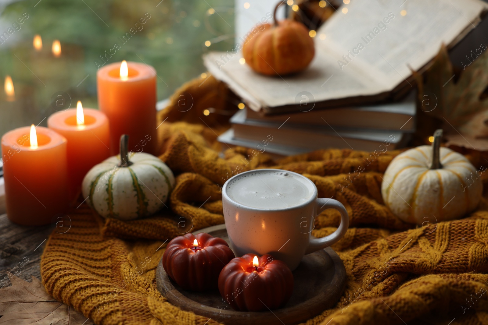 Photo of Cup of coffee, pumpkins, burning candles and soft sweater on table. Autumn atmosphere