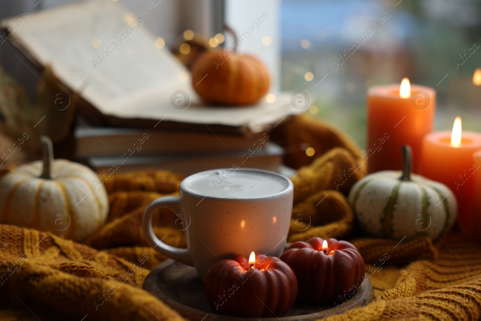 Photo of Cup of coffee and burning pumpkin shaped candles on soft sweater. Autumn atmosphere