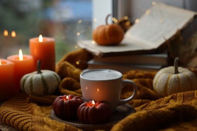 Photo of Cup of coffee, burning pumpkin shaped candles and soft sweater on table. Autumn atmosphere