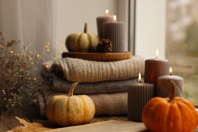 Photo of Burning candles, open book and stack of soft sweaters on windowsill. Autumn atmosphere