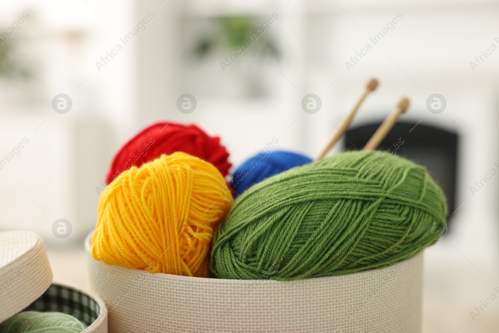 Photo of Colorful yarns and knitting needles in box on blurred background, closeup