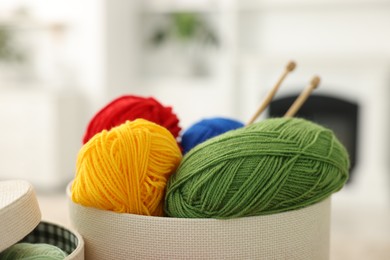 Photo of Colorful yarns and knitting needles in box on blurred background, closeup