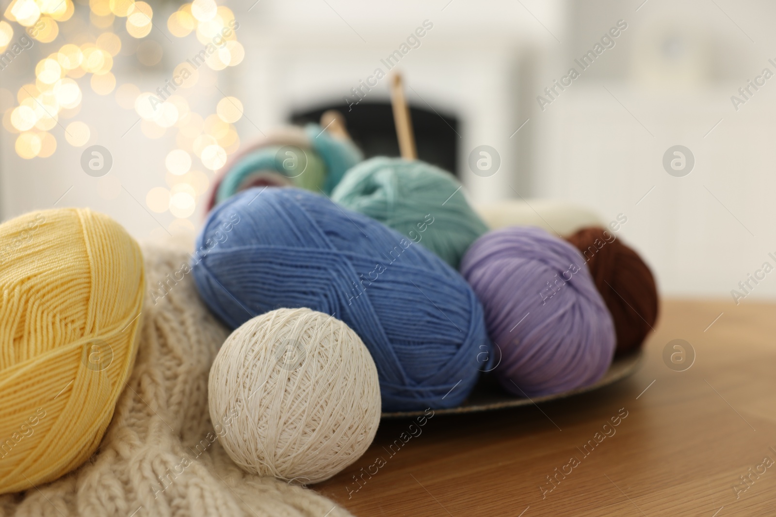 Photo of Colorful yarns and pattern sample on wooden table against blurred lights, closeup