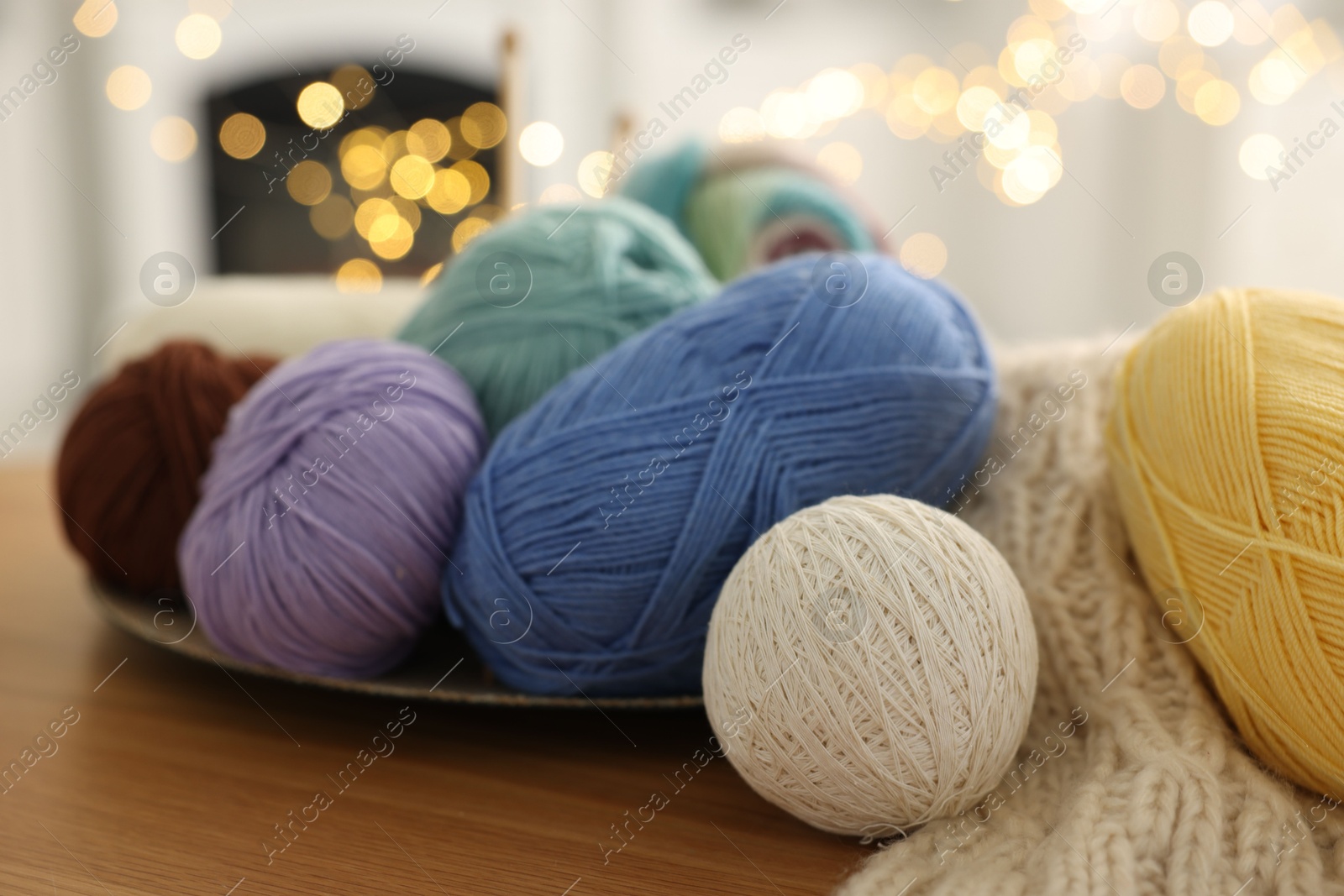 Photo of Colorful yarns and pattern sample on wooden table against blurred lights, closeup