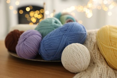 Photo of Colorful yarns and pattern sample on wooden table against blurred lights, closeup