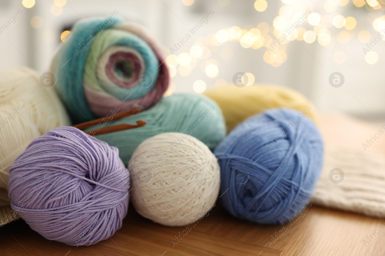 Photo of Colorful yarns and crochet hooks on wooden table against blurred lights, closeup