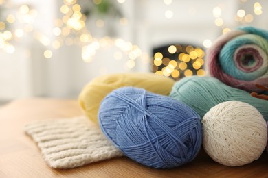 Photo of Colorful yarns and pattern sample on wooden table against blurred lights, closeup. Space for text