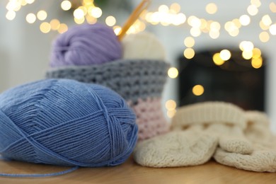 Photo of Colorful yarns and knitted mittens on wooden table against blurred lights, closeup