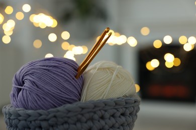 Photo of Basket with colorful yarns and crochet hooks against blurred lights, closeup