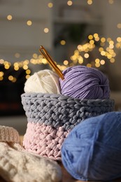 Basket with colorful yarns and crochet hooks against blurred lights, closeup