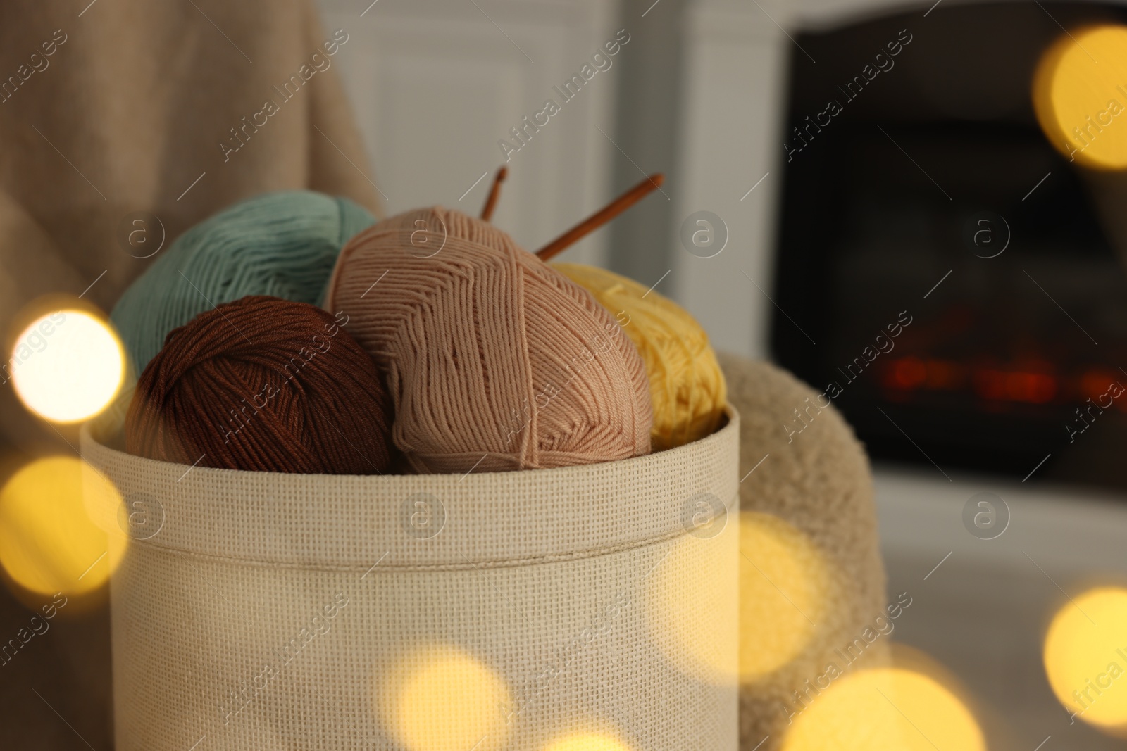 Photo of Box with colorful yarns and crochet hooks indoors among blurred lights, closeup