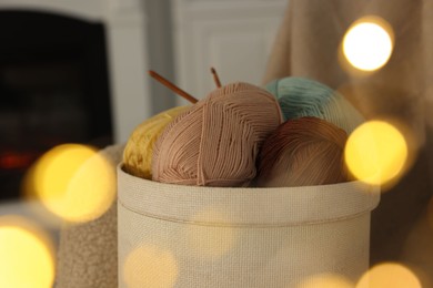 Photo of Box with colorful yarns and crochet hooks indoors among blurred lights, closeup