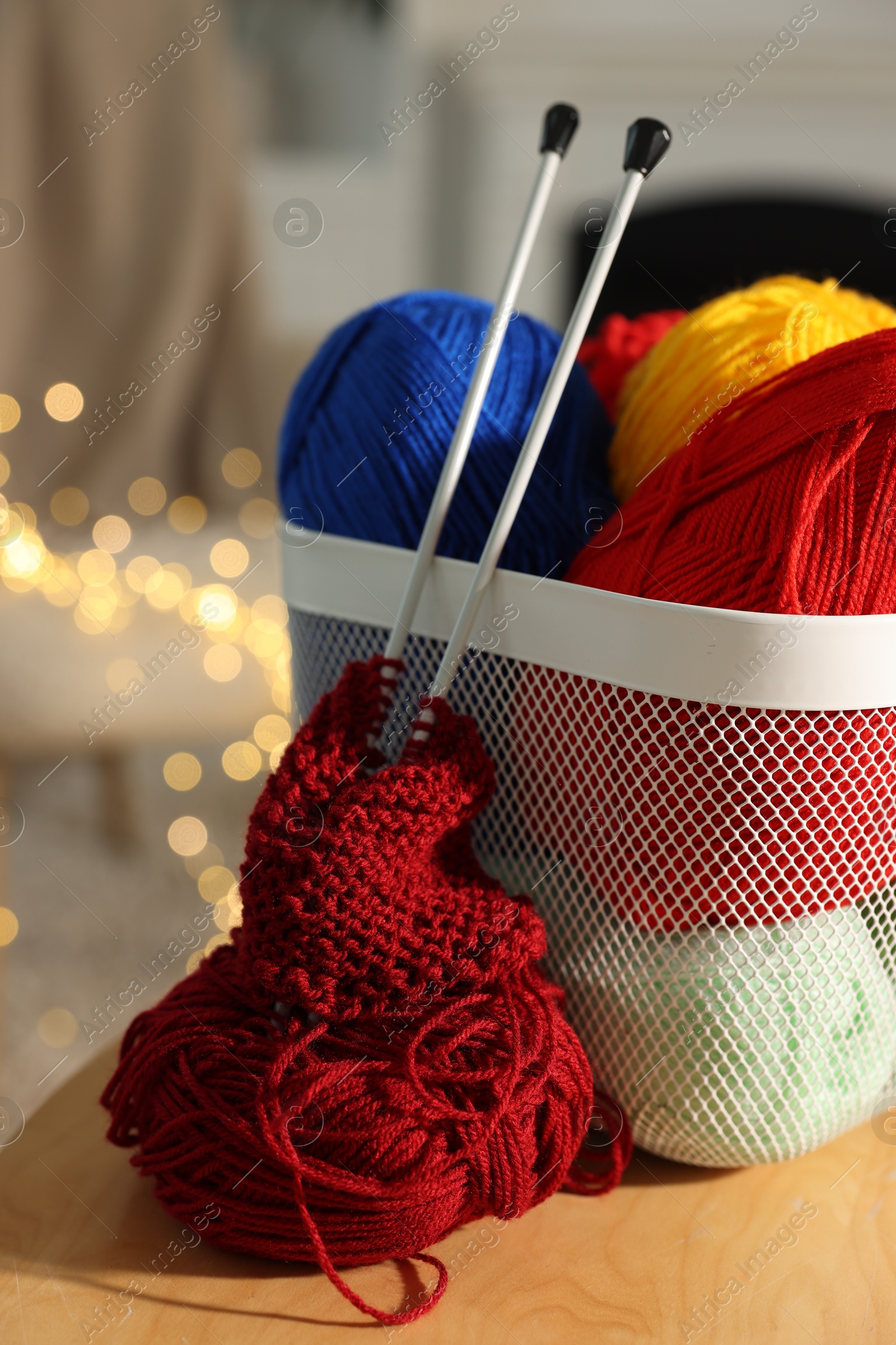 Photo of Colorful yarns, knitting needles, pattern sample and basket on wooden table indoors, closeup