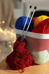 Photo of Colorful yarns, knitting needles, pattern sample and basket on wooden table indoors, closeup