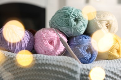 Photo of Many colorful yarns and crochet hook on blanket among blurred lights, closeup