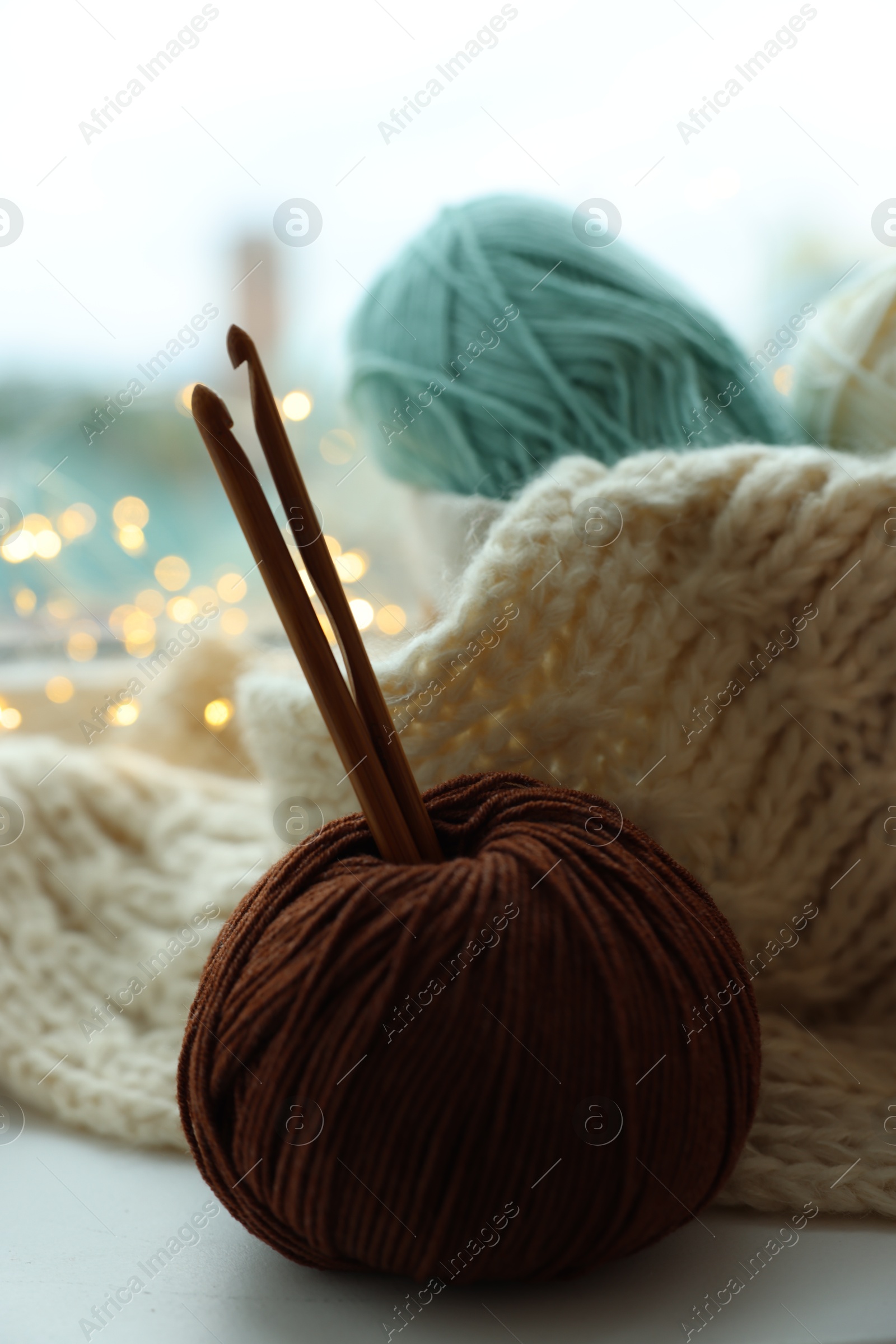 Photo of Yarn, crochet hooks and sweater on table indoors, closeup