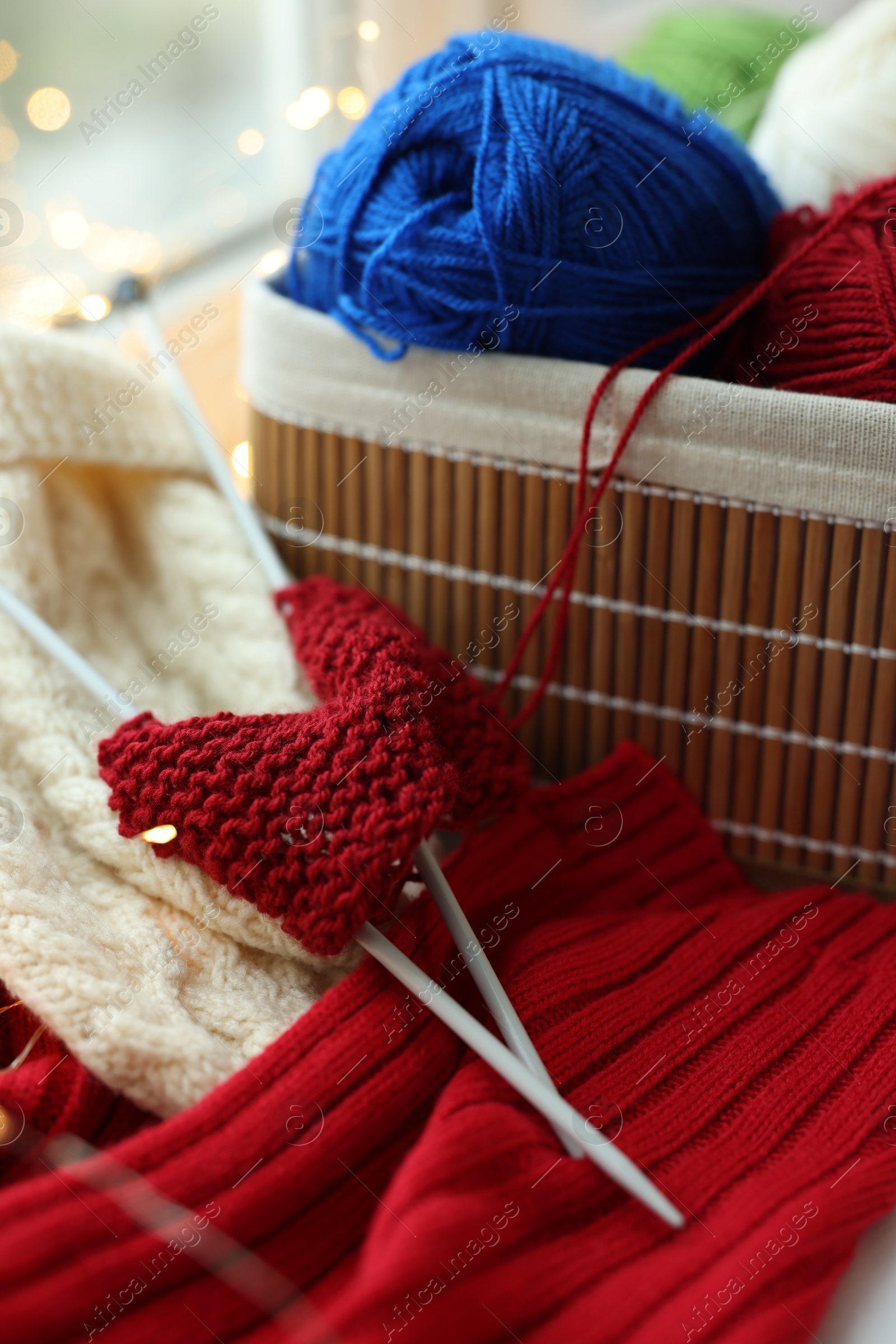 Photo of Colorful yarns, knitting needles, mittens and pattern sample on blurred background, closeup