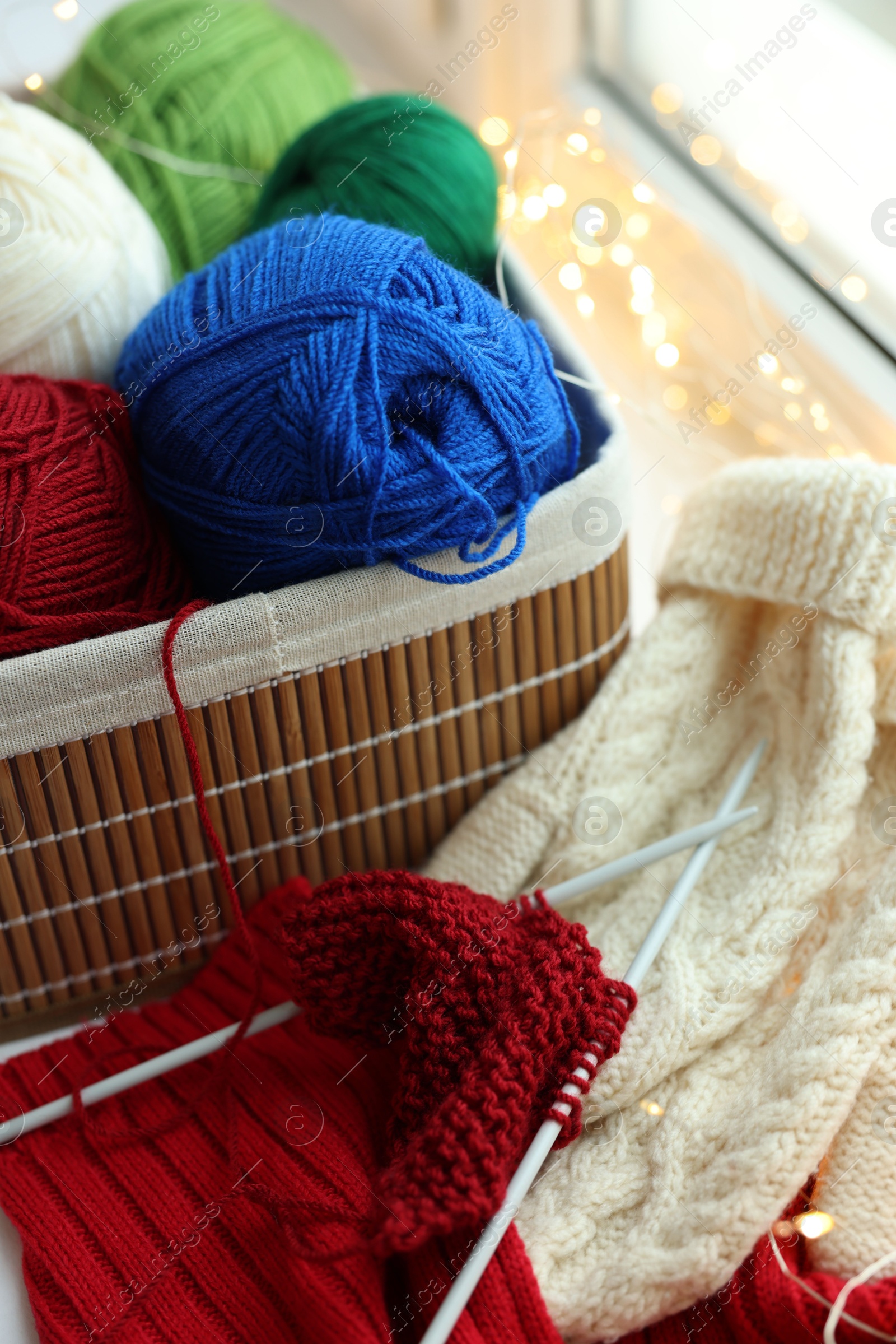 Photo of Colorful yarns, knitting needles, mittens and pattern sample on blurred background, closeup