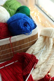 Photo of Colorful yarns, knitting needles, mittens and pattern sample on blurred background, closeup