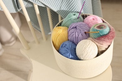 Photo of Box with colorful yarns and crochet hooks on chair indoors