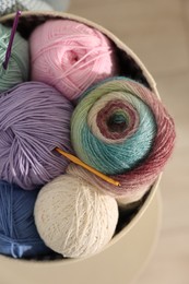 Photo of Box with colorful yarns and crochet hooks on blurred background, top view