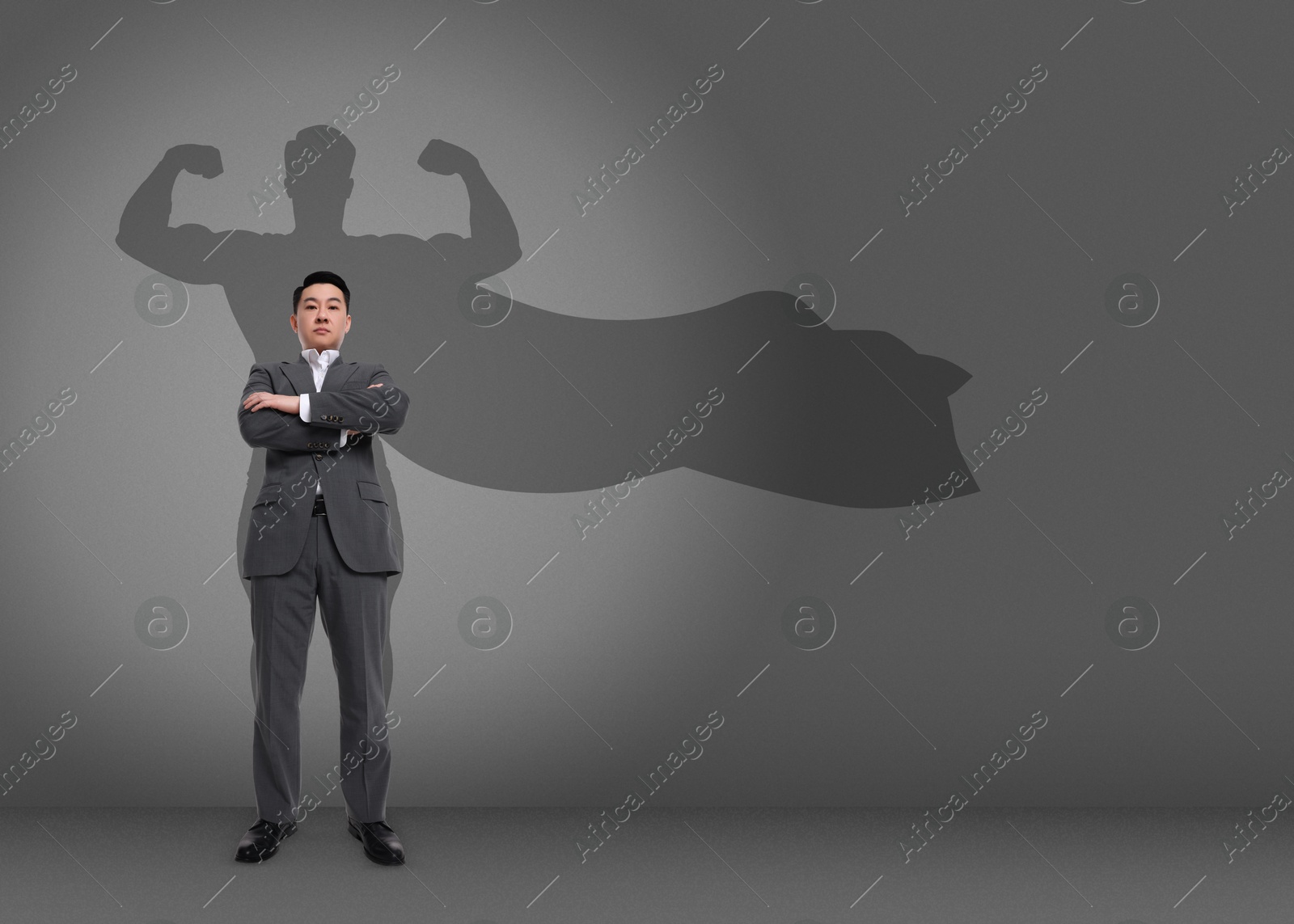 Image of Confident businessman casting shadow of superhero on grey background. Success, power, leadership and determination concepts