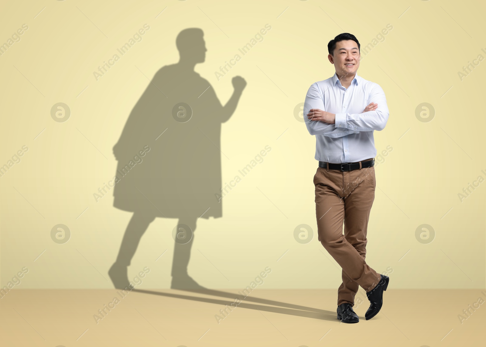 Image of Confident businessman casting shadow of superhero on pale yellow background. Success, power, leadership and determination concepts