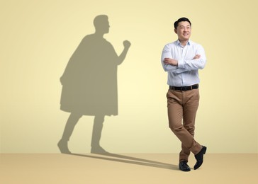 Image of Confident businessman casting shadow of superhero on pale yellow background. Success, power, leadership and determination concepts