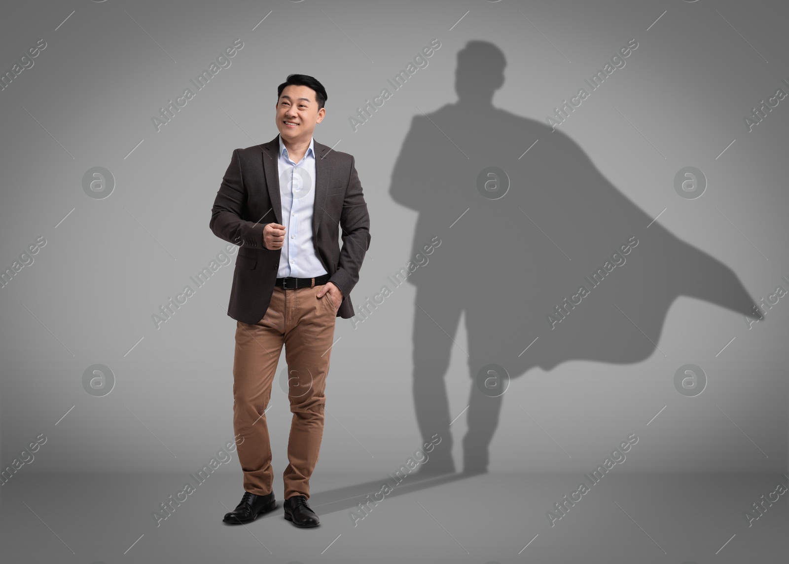 Image of Confident businessman casting shadow of superhero on grey background. Success, power, leadership and determination concepts