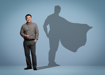 Confident businessman casting shadow of superhero on light blue background. Success, power, leadership and determination concepts