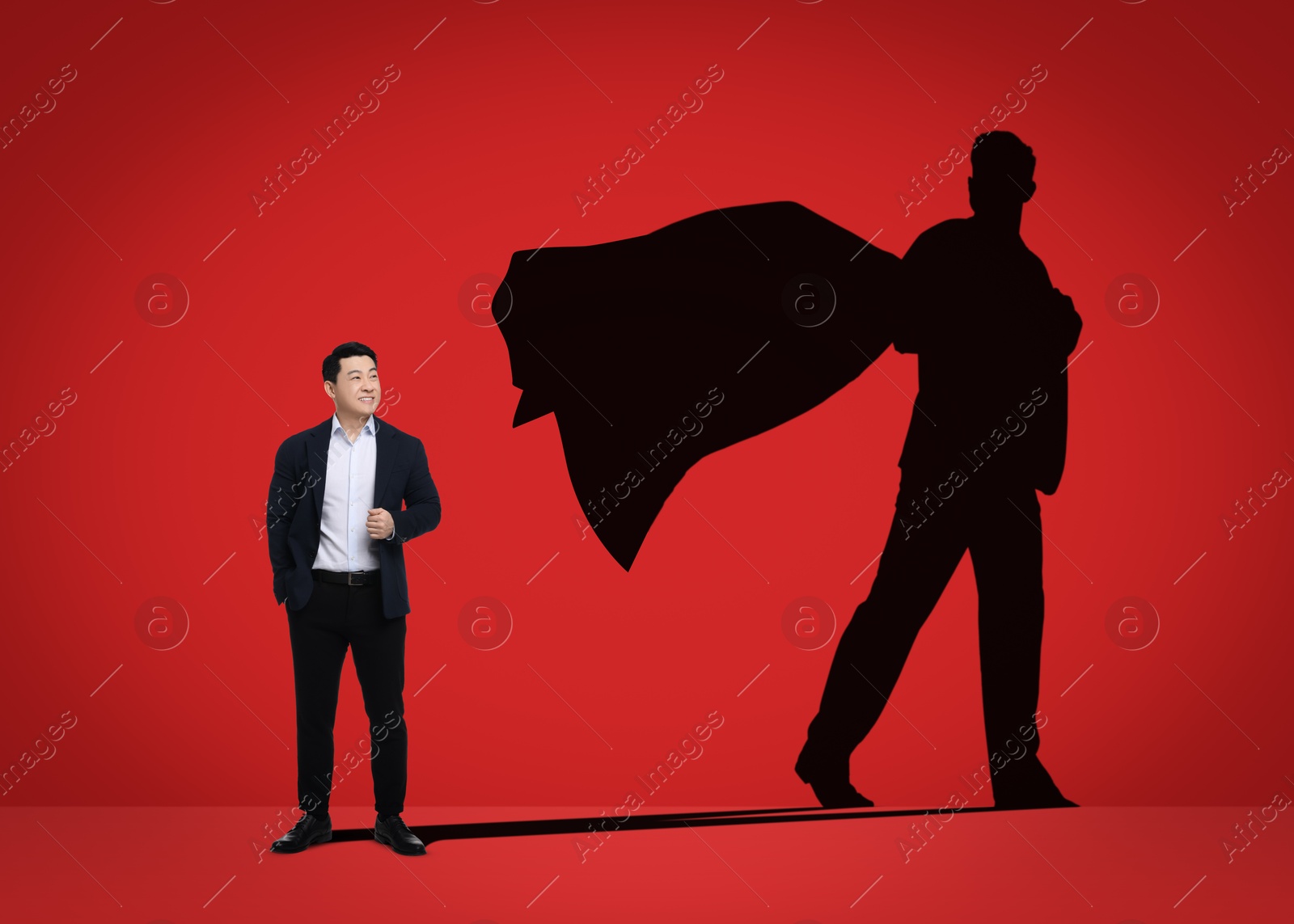 Image of Confident businessman casting shadow of superhero on red background. Success, power, leadership and determination concepts