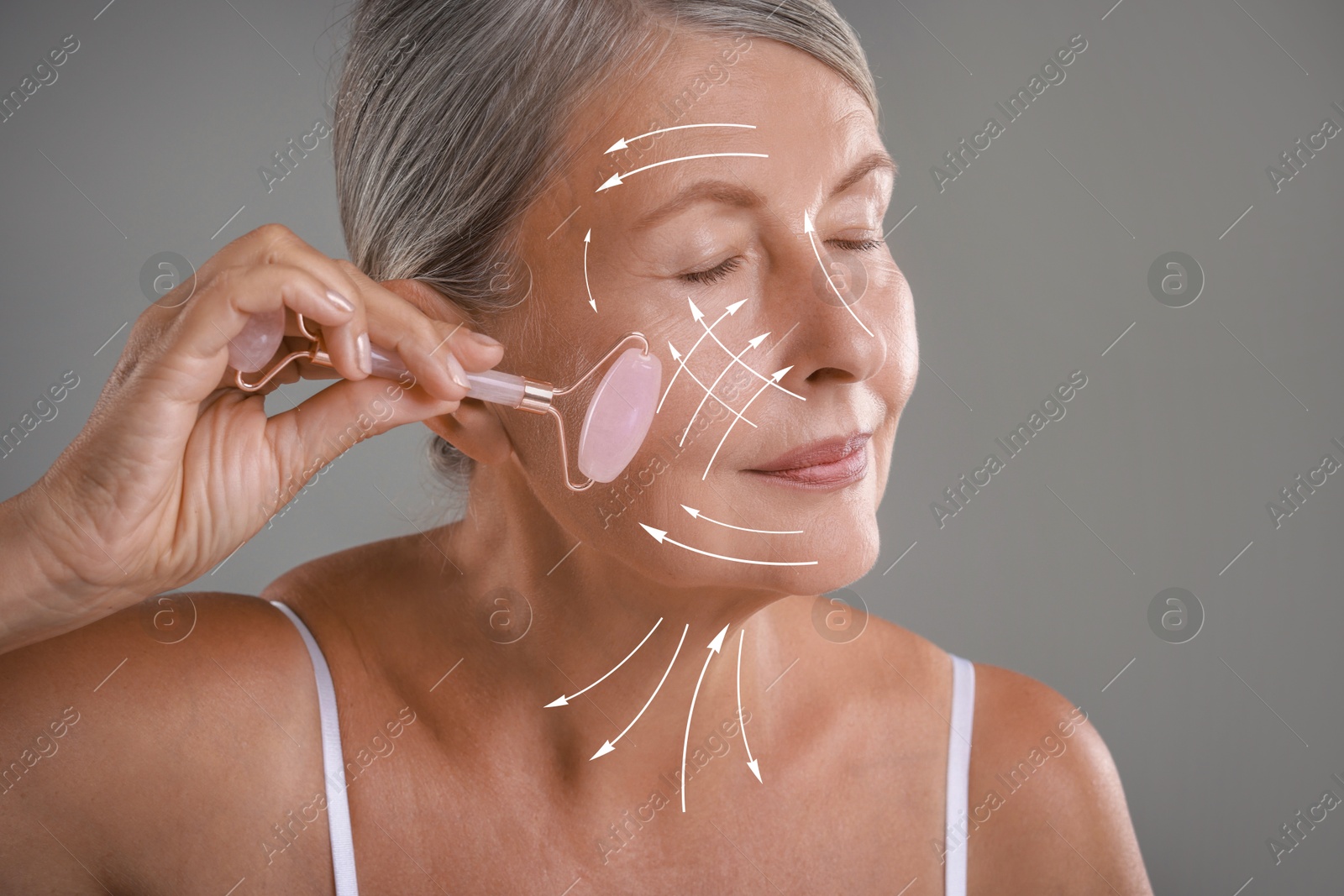 Image of Beautiful woman doing facial massage with roller on grey background. Arrows on skin showing direction of moves