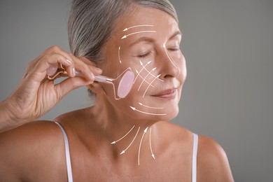 Beautiful woman doing facial massage with roller on grey background. Arrows on skin showing direction of moves