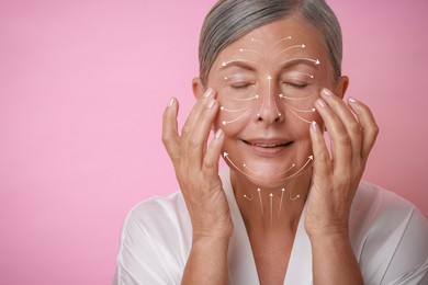 Image of Beautiful woman doing facial massage on pink background. Arrows on skin showing direction of moves