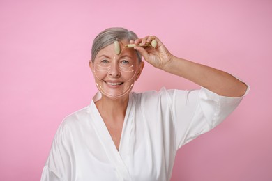 Beautiful woman doing facial massage with roller on pink background. Arrows on skin showing direction of moves