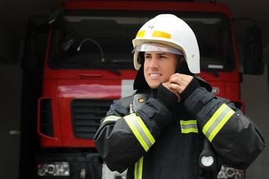 Firefighter in uniform wearing helmet near fire truck at station, space for text