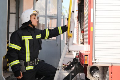 Firefighter in uniform and helmet near fire truck at station