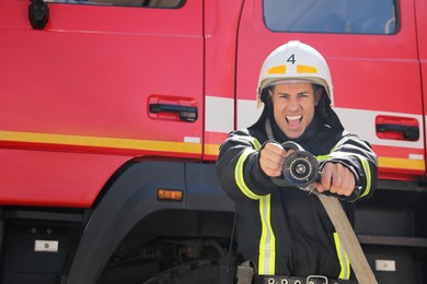 Photo of Firefighter in uniform with high pressure water jet near fire truck outdoors