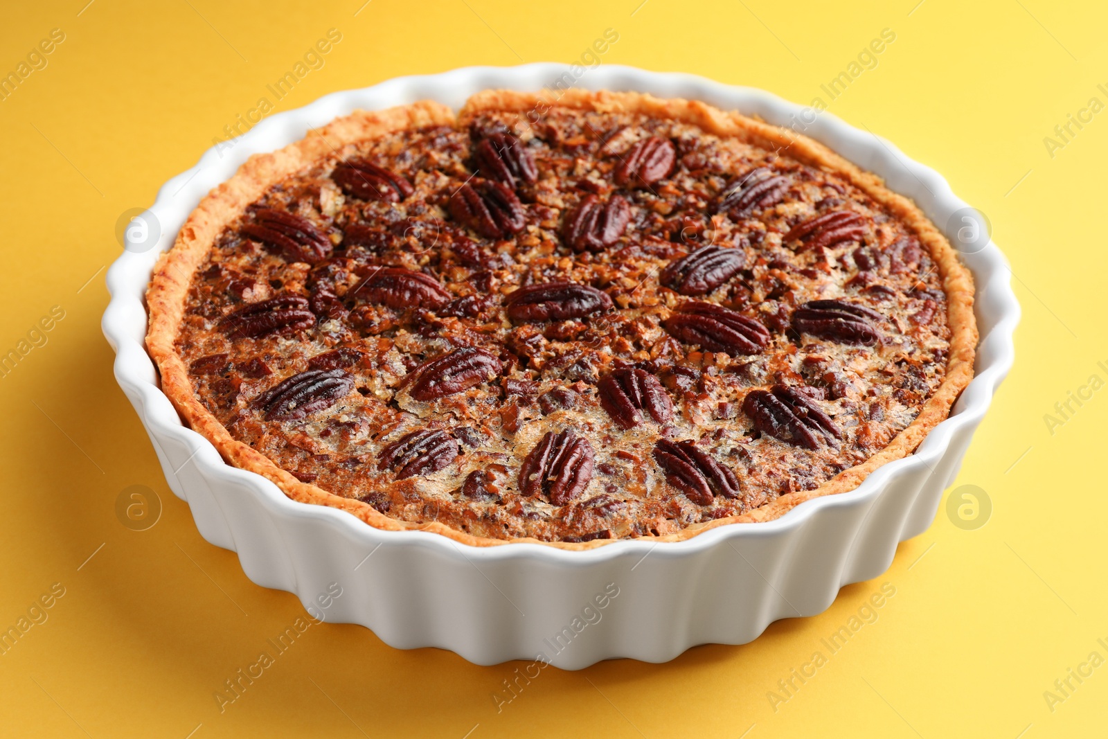 Photo of Delicious pecan pie in baking dish on yellow background, closeup