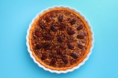 Photo of Delicious pecan pie in baking dish on light blue background, top view