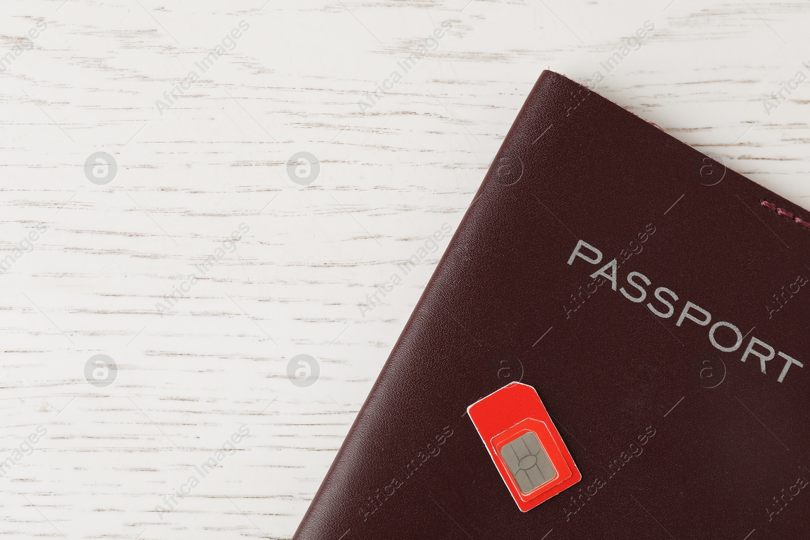 Photo of Passport and SIM card on white wooden table, top view. Space for text