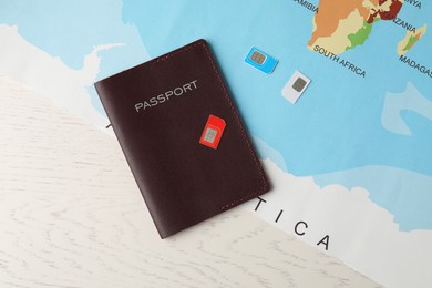 Photo of Passport, world map and SIM cards on white wooden table, flat lay