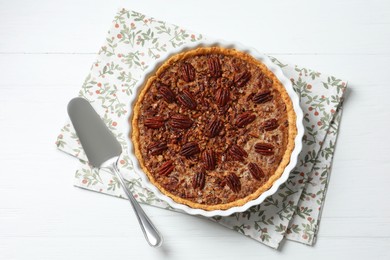 Photo of Delicious pecan pie in baking dish and cake server on white wooden table, flat lay