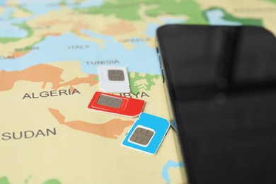 Photo of SIM cards and smartphone on world map, closeup