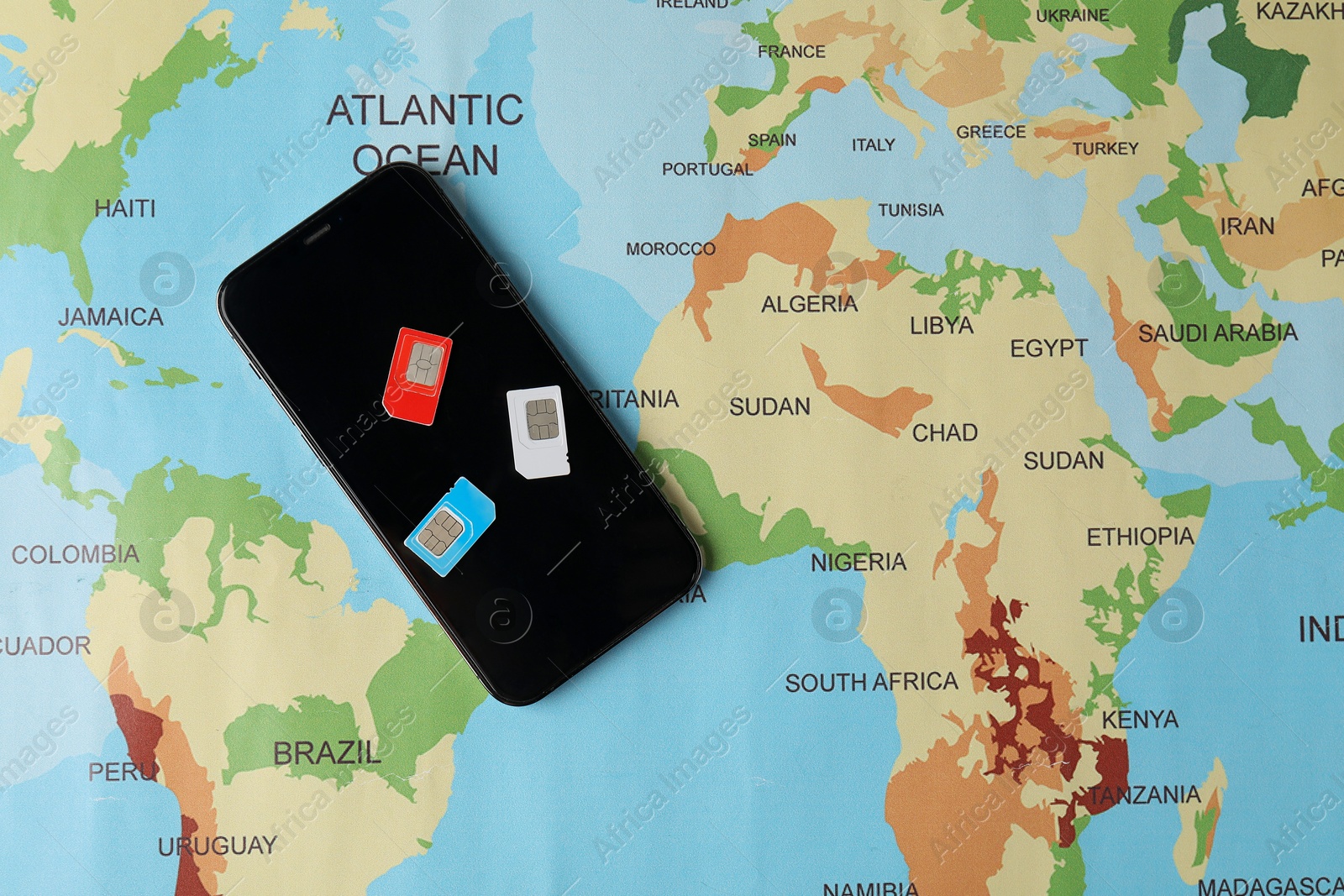 Photo of SIM cards and smartphone on world map, flat lay