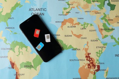 SIM cards and smartphone on world map, flat lay