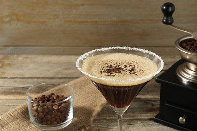 Glass of fresh cocktail, manual coffee grinder and beans in bowl on wooden table, closeup