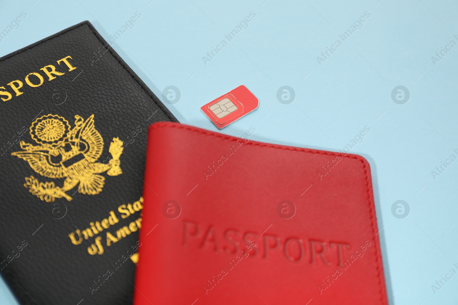 Photo of Modern SIM card and passport on light blue background, closeup