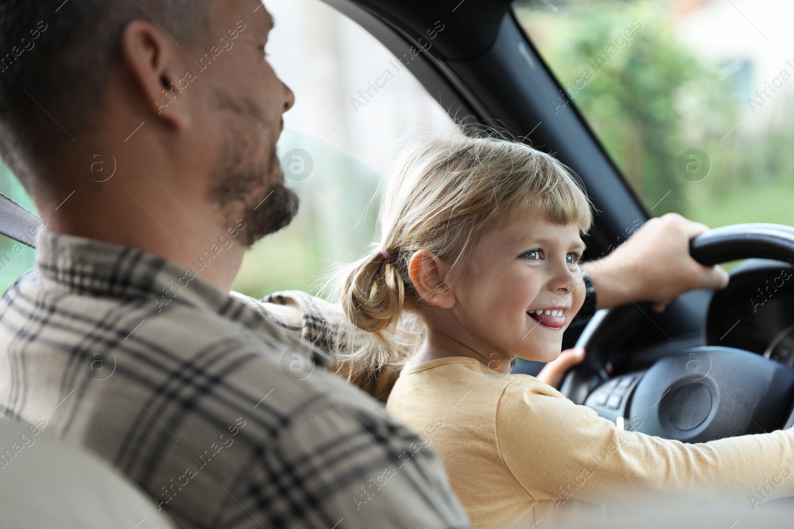 Photo of Man with his daughter holding steering wheel inside car