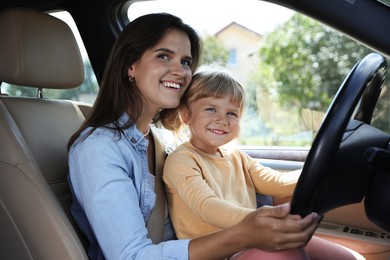 Photo of Happy woman with her daughter holding steering wheel inside car